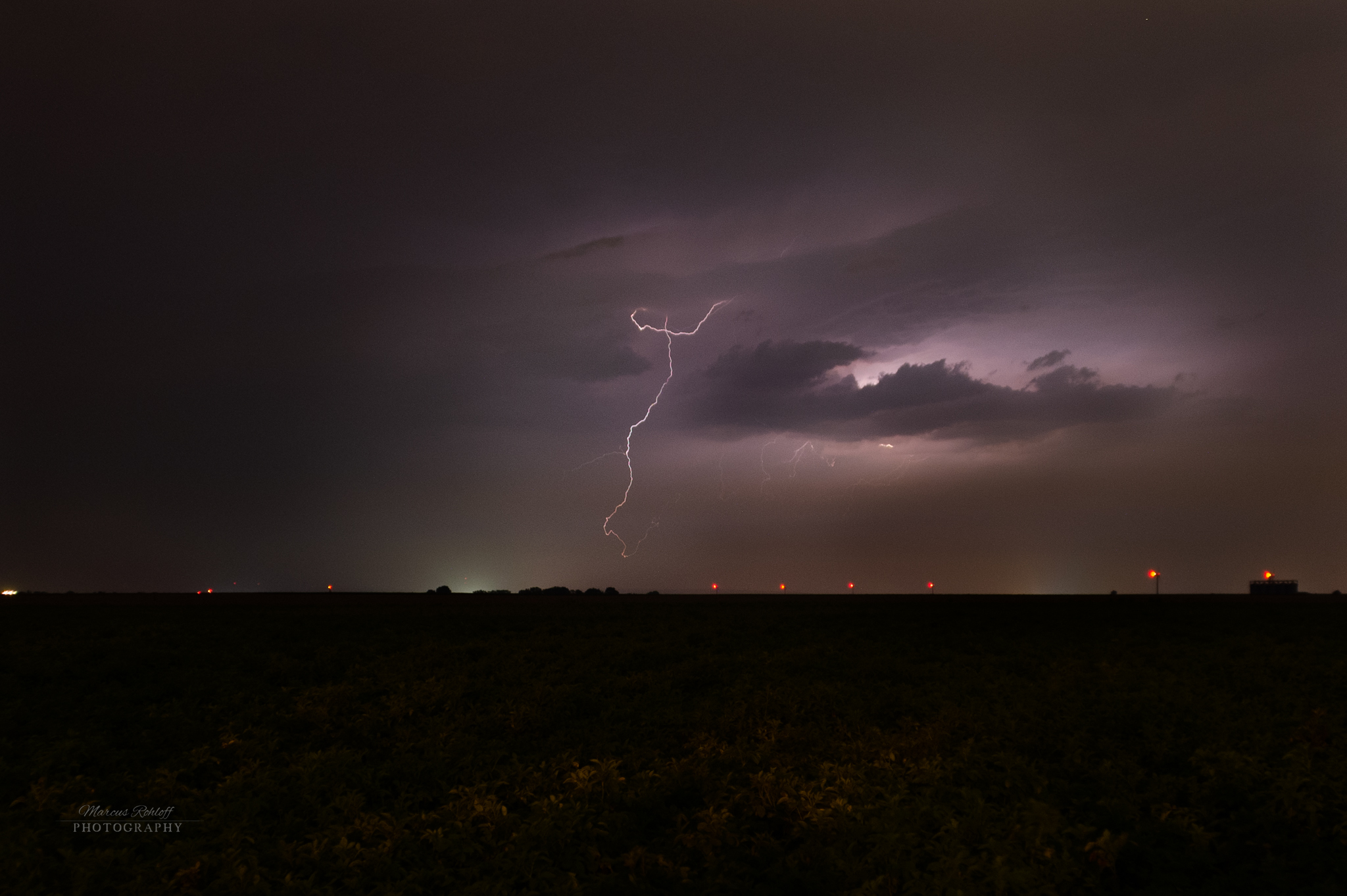 Dieses Bild ist eine Langzeitbelichtung während eines Gewitters bei Nacht und zeigt einen geschwungenen Blitz mit einem lilanen Farbakzent.